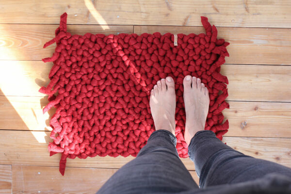 Teppich aus Schafwolle rot auf Holzboden, Füße auf dem Teppich, Merinowolle aus Deutschland